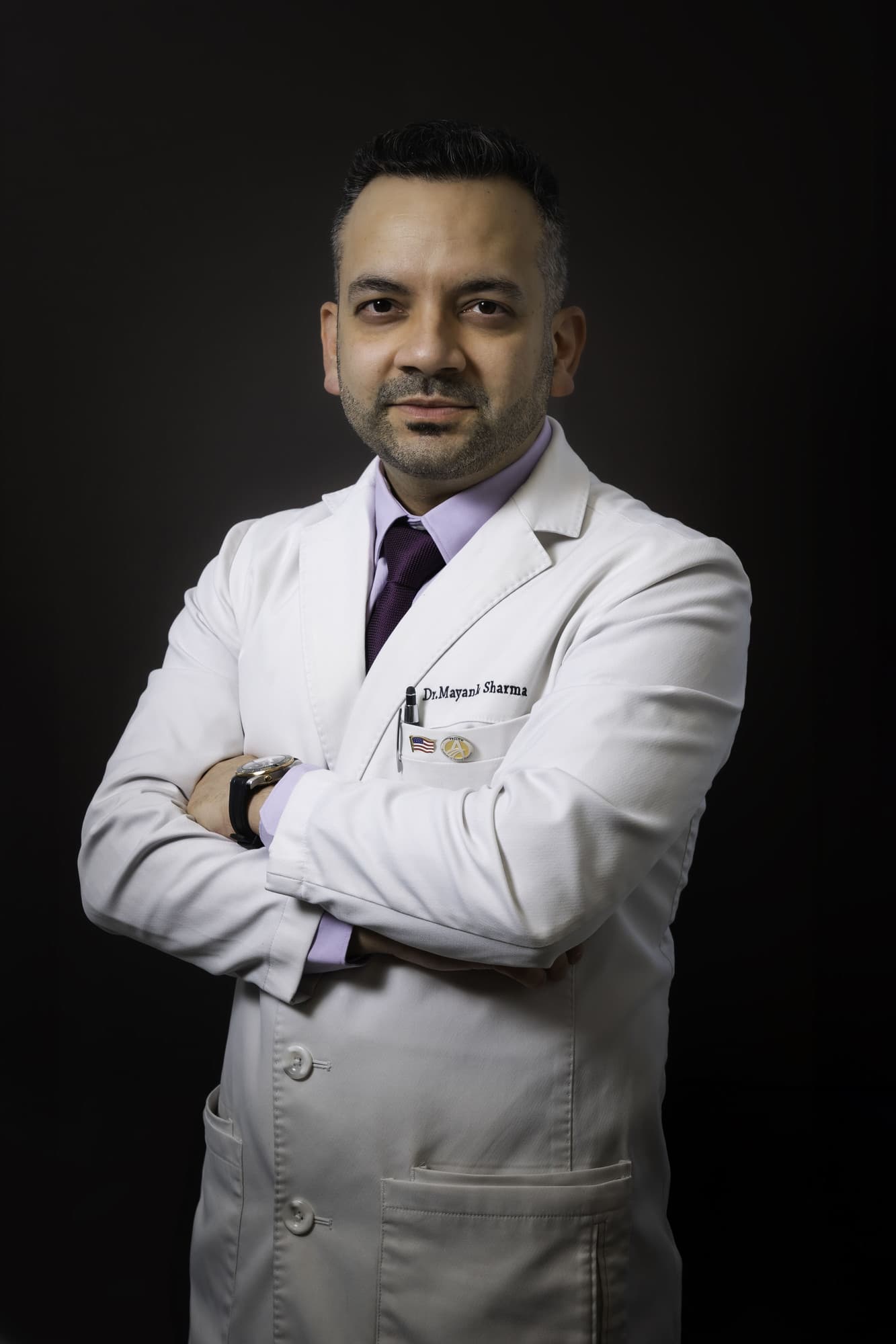 Dr. Mayank Sharma, DDS, FAGD, FICD, in a white dental coat, confidently posing with arms crossed, showcasing his expertise in advanced general, cosmetic, and implant dentistry.