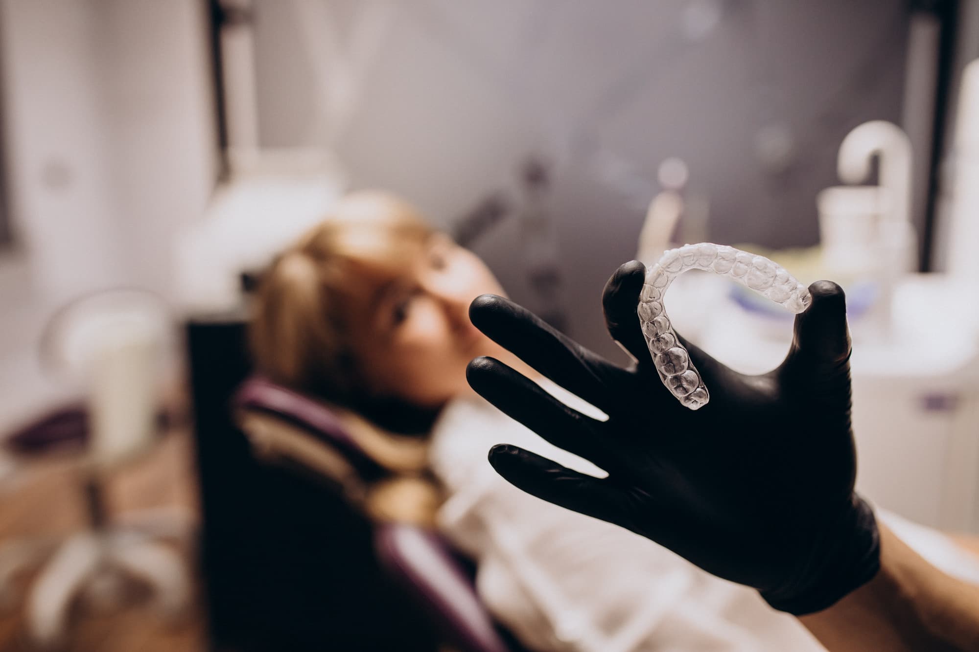 Dental professional wearing black gloves preparing to assist a patient in a dental office, highlighting custom night guard consultation for bruxism treatment.